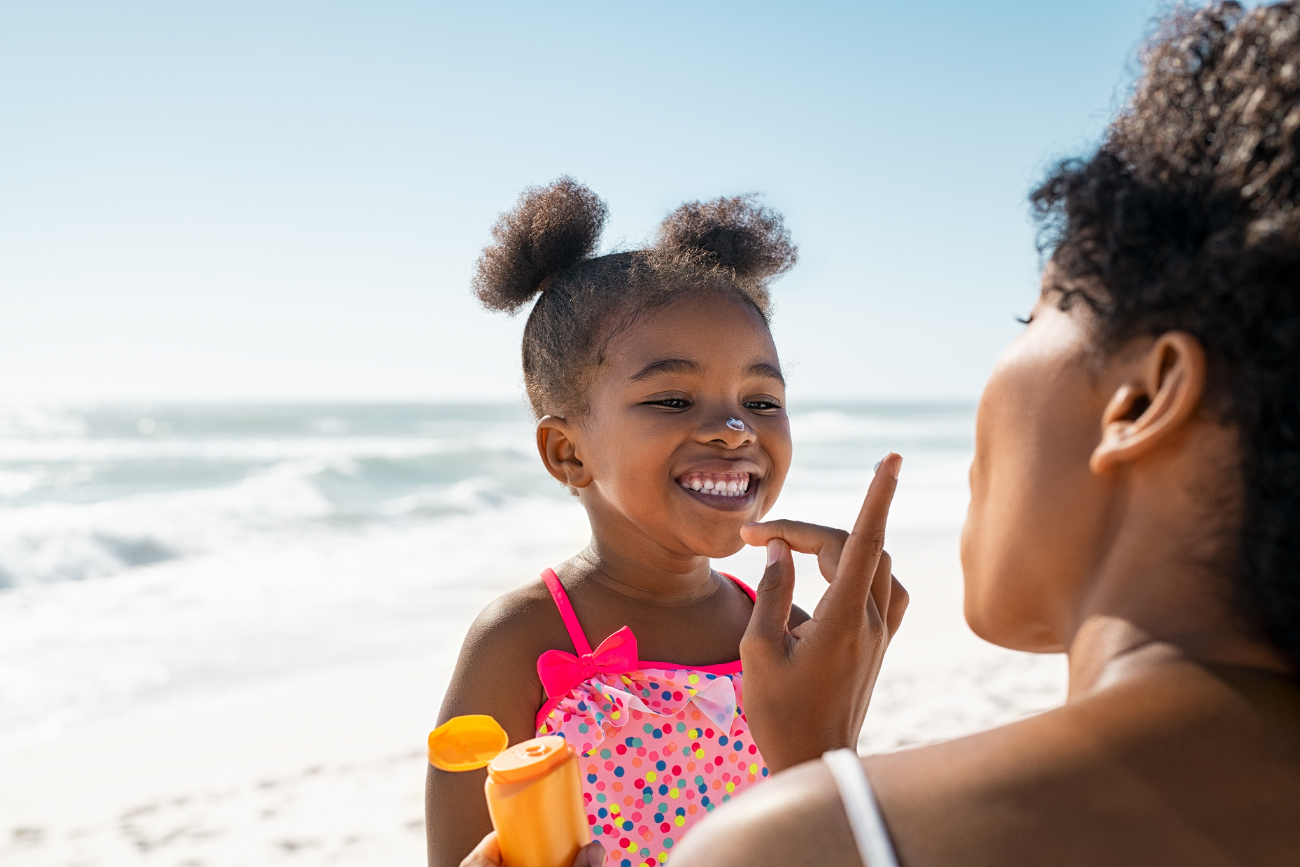 mom applying sunscreen to dark skinned black daughter at beach summer spring tips prevention skin sunburn