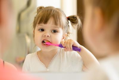 young girl brushing teeth in mirror early dental care little kid