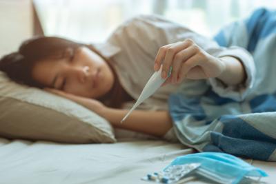 sick teen in bed holding up a thermometer with mask Mononucleosis mono fever illness